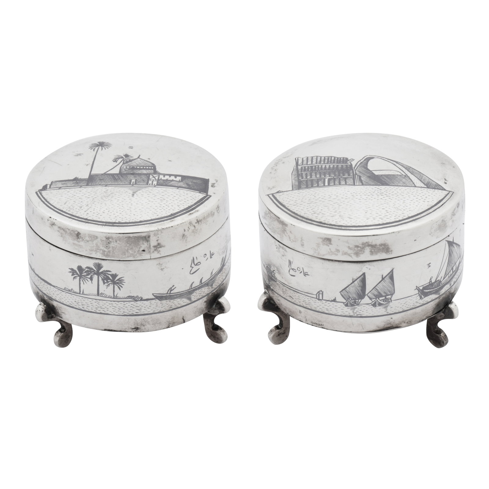 Omara circa 1930, signed Salih A pair of early 20th century Iraqi silver and niello dressing table: Omara circa 1930, signed Salih A pair of early 20th century Iraqi silver and niello dressing table jars Each of cylindrical form with pull off gently domed lids, raised upon three scroll feet. One lid