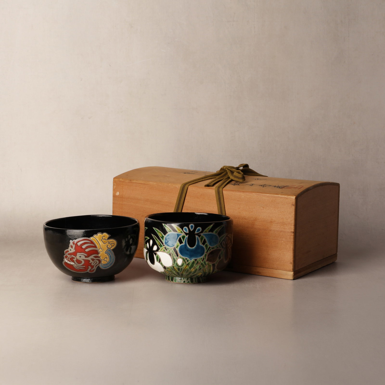 Two Japanese Kyoto ware tea bowls, manner of Ogata Kenzan (Japanese, 1663?1743): Two chawan tea bowls, worked in the manner of Ogata Kenzan, comprising, one bowl painted in Noh masks in yellow, green and red; and another painted with irises in blue, white and purple with green lea