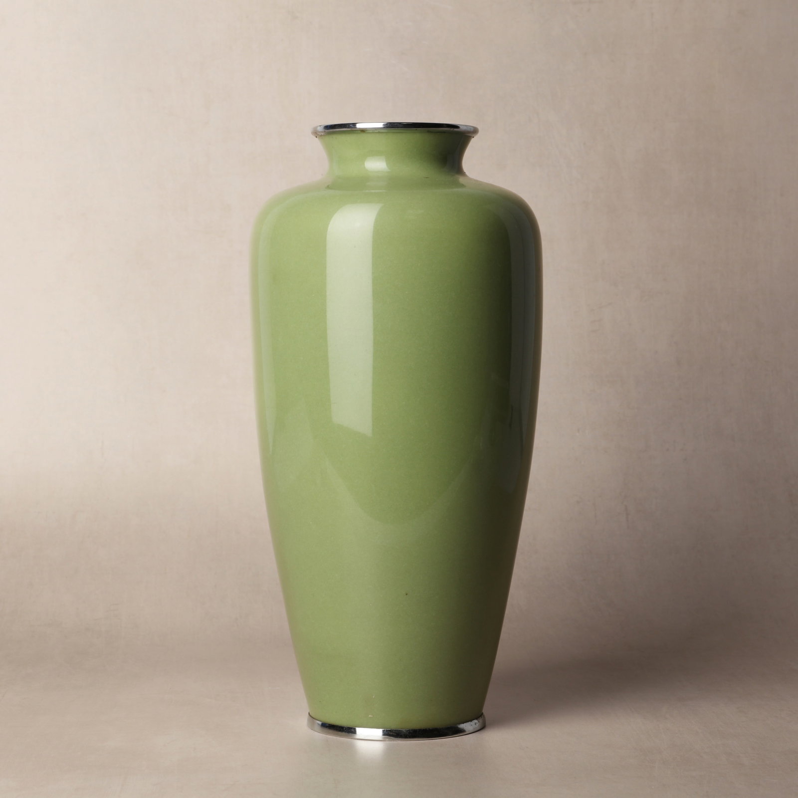 A Japanese cloisonne enamel 'prunus' vase, 19th/20th century: The tall vase decorated on a green-ground with a large flowering prunus branch at the center, with white metal mounts Size:(27cm high) Qty: (1)