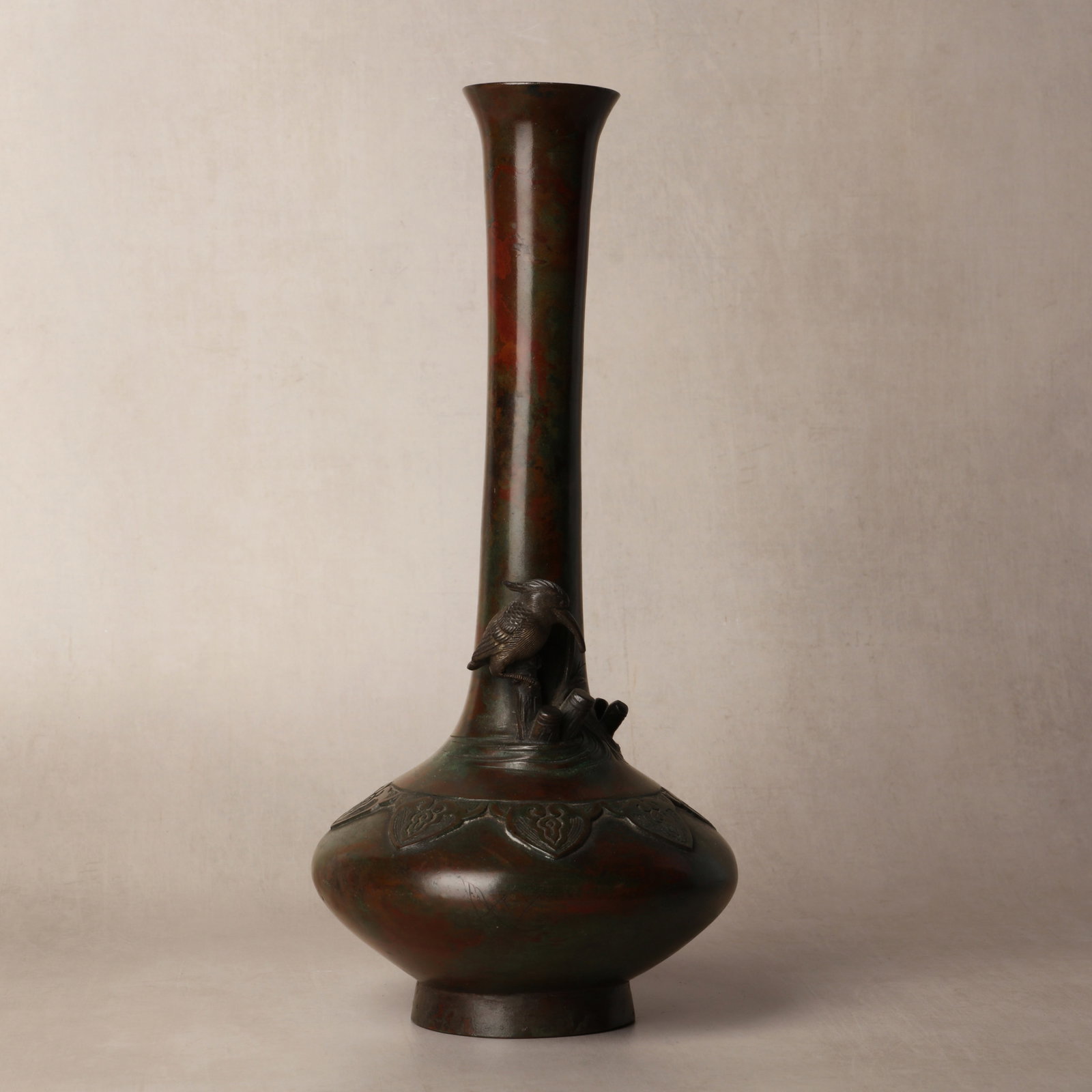 A Japanese bronze 'kingfisher' vase, 19th century: Formed with a solitary kingfisher perched atop stems protruding from the water, all on a compressed body cast in relief with lappets rising to an elongated neck with a flared rim, the base with a fain
