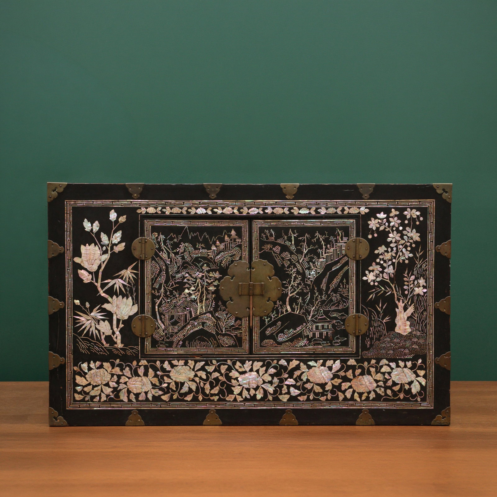 A fine Korean mother-of-pearl inlaid lacquered wood chest, Joseon dynasty, 19th century: The large lacquered wood chest of rectangular form, with brass hinged doors fitted with a brass lock and pin, the front, top and sides all decorated with inlaid mother-of-pearl against the dark browni