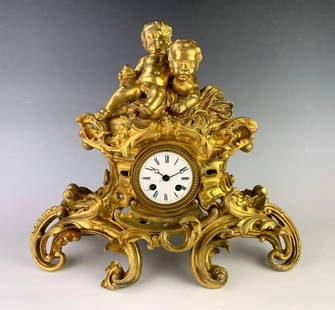 French Dore Bronze 2 Putti Clock C. 1880: Depicting two putti sitting atop an ornate gilt bronze case, has French movement with pendulum and key, good condition, dial has chipping around key hole, 15" x 17" *All clocks are sold as is and are