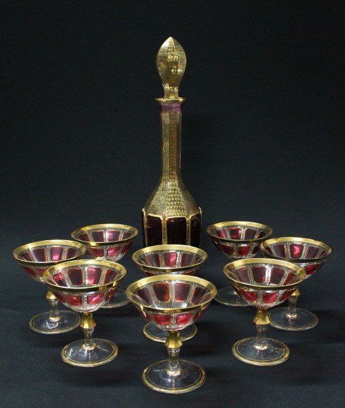 A MOSER CRANBERRY GLASS DRINK SET: A Moser Cranberry Glass Drink Set, gilt borders and accents throughout, comprising a stoppered decanter and eight stems with shaped and faceted standards. H 16 5/8.