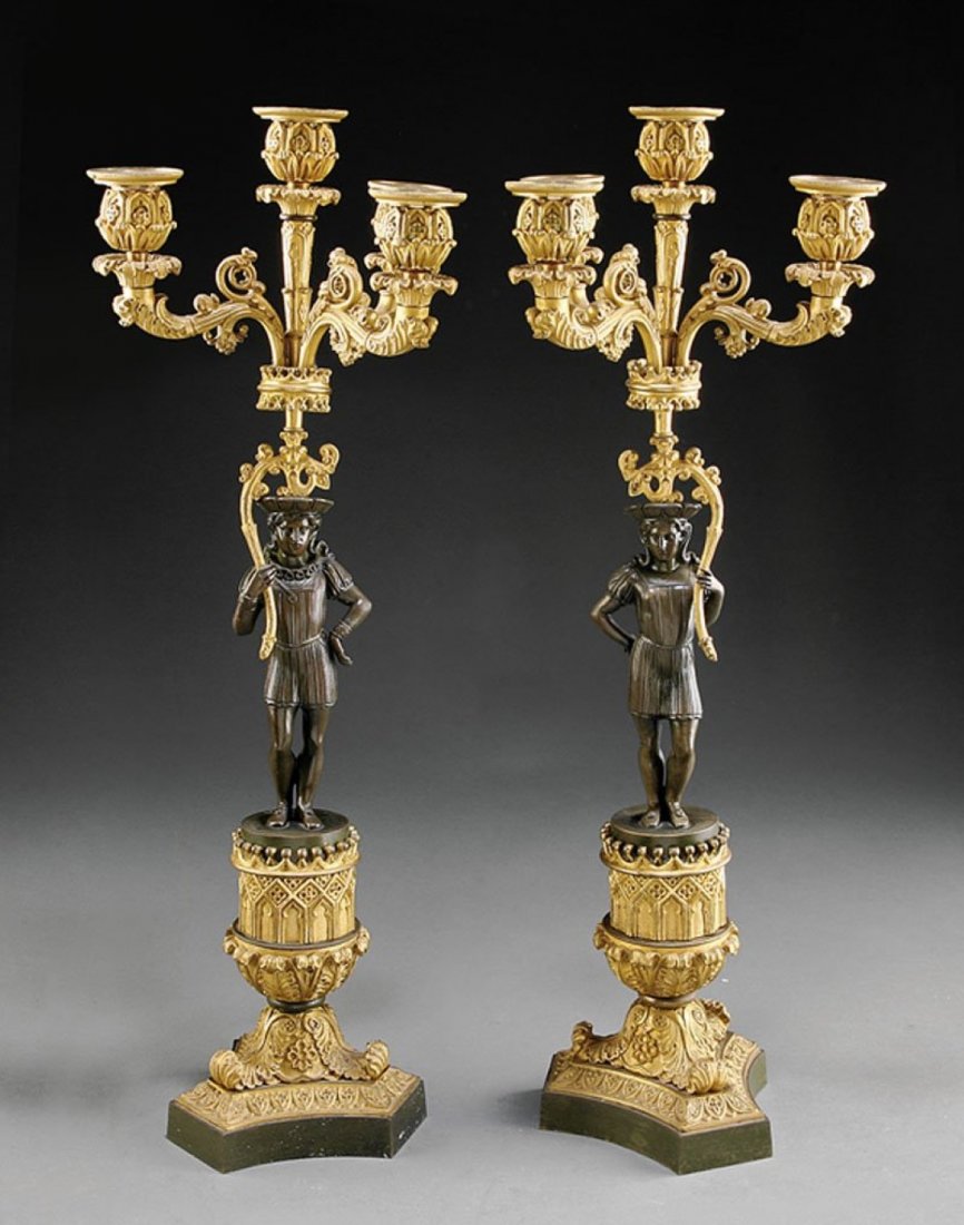 Patinated Gilt Bronze Four-Light Candelabra: A Pair of French Gothic Patinated and Gilt Bronze Figural Four-Light Candelabra, mid-19th c., each with a standing medieval figure supporting scrolling candlearms, tracery pedestal on foliate scrolls,