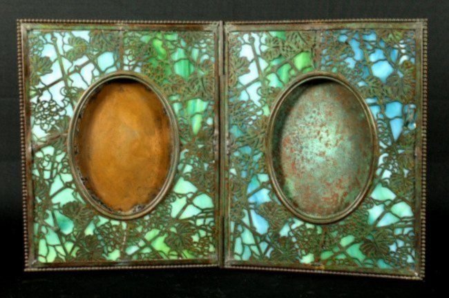 RARE TIFFANY STUDIO NEW YORK HINGED DOUBLE PICTURE: RARE TIFFANY STUDIO NEW YORK HINGED DOUBLE PICTURE FRAME. OPENWORK FLORAL DECORATION OVER BLUE GLASS. SIGNED AND NUMBERED 854. MEASURES H: 10" W: 7 7/8". OPEN 15 3/4"