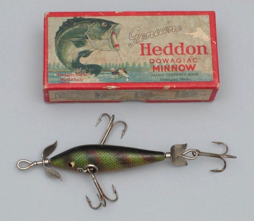 Heddon No. 100 Dowagiac Minnow in Up Leaping Bass Box: Possessing glass eyes, marked props, L--rig hardware and perch finish. In Very Good plus condition with light varnish flaking, a few minor finish chips. Box is marked 109L and has some minor paper los