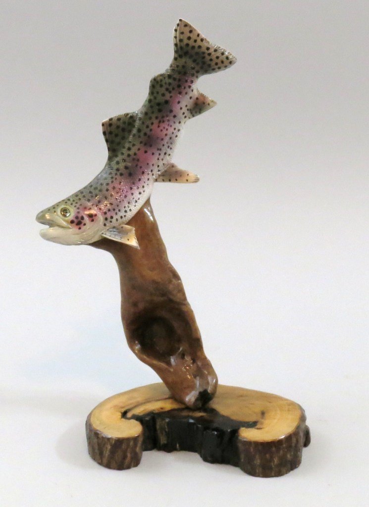 Driftwood Carving of a Rainbow Trout by Jim Wiley: Measuring 12 3/4" x 7 1/2" of a stylized swimming rainbow trout on a persimmon base. Signed by the carver with his code "1212", carved in 2012 and the twelfth carving of that year. This contemporary c