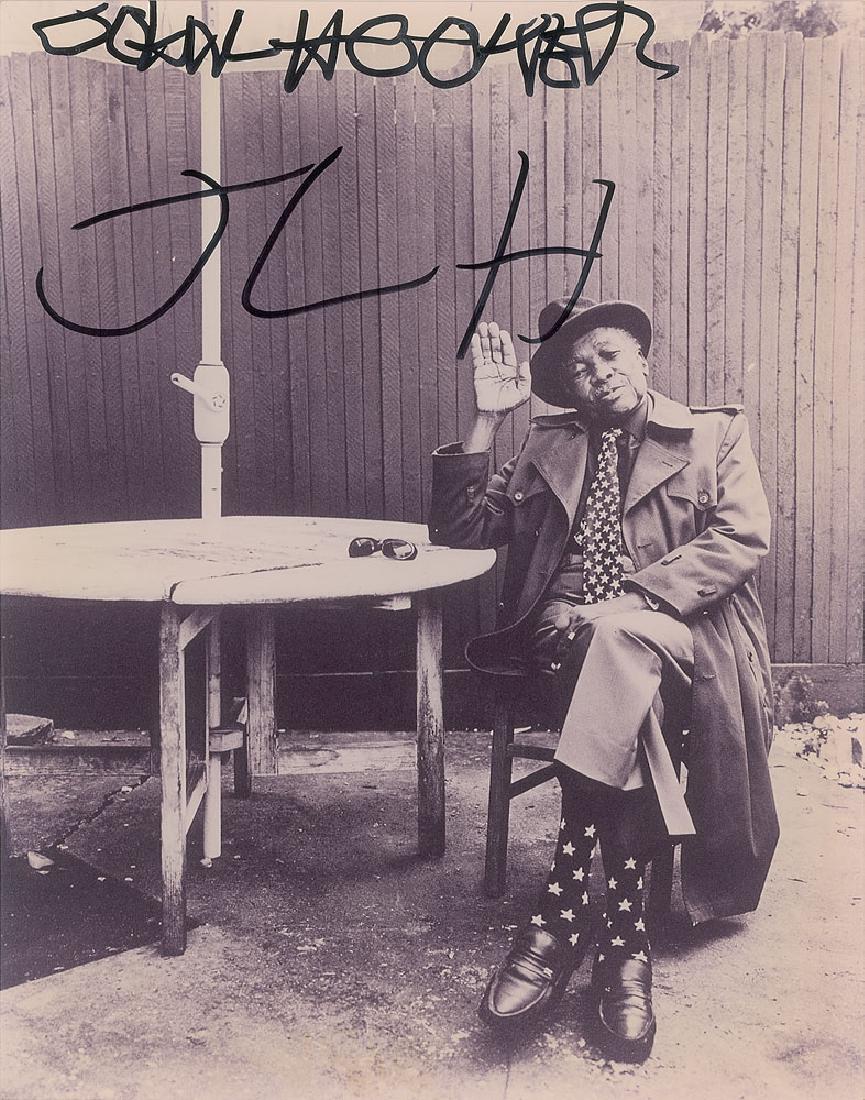 John Lee Hooker Oversized Signed Photograph: Glossy 11 x 14 full-length photo of Hooker seated outside and waving, signed in black felt tip, "John L. Hooker, JLH." In fine condition.
