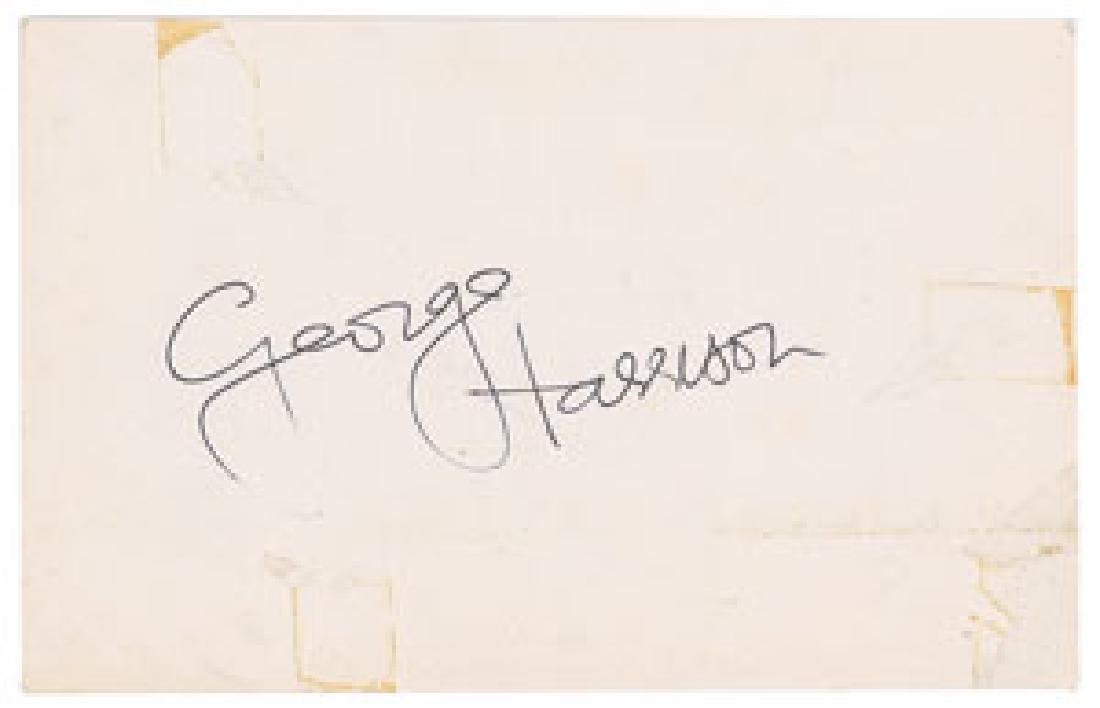 George Harrison Signed Photo Postcard: Glossy 3.5 x 5.5 close-up postcard photo of Harrison, boldly signed on the reverse in black ballpoint, "George Harrison." In very good condition, with tape stains and tape-related surface loss (all ea
