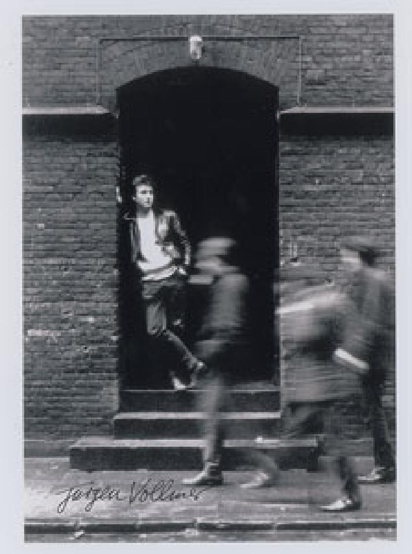 John Lennon Photograph by Jurgen Vollmer: Modern glossy 8.25 x 11 photographic print of John Lennon originally taken by photographer Jürgen Vollmer, who signs below in black felt tip. The image features Lennon standing in a doorway at Jager-