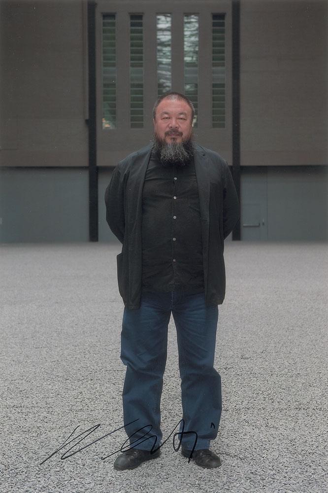 Ai Weiwei: Color satin-finish 8 x 12 photo of Ai Weiwei posing amidst millions of his hand-painted porcelain sunflower seeds, signed in black felt tip. In very fine condition. Format: Signed Photo