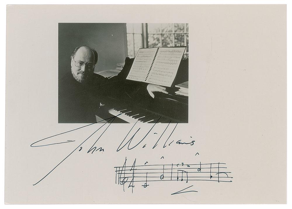 John Williams: Glossy 7 x 5 photo of Williams at his keyboard, signed in the wide lower margin in black felt tip, "John Williams," with a musical quote from his iconic Star Wars theme. In fine condition. Format: AMQ
