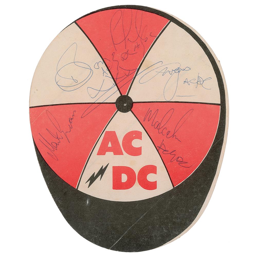 AC/DC Signed Logo Sticker: Uncommon vintage AC/DC logo sticker with a baseball cap design, 5 x 6, signed in blue ballpoint by Bon Scott, Malcolm Young, Angus Young, Phil Rudd, and Mark Evans, all but Evans signing with just the