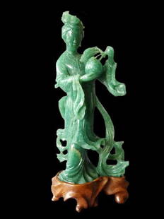 Green Jade Female Attendant, 20th Century: Green Jade Female Attendant, 20th Century. The green colored stone finely carved depicting a female attendant attired in a long flowing dress and holding a large fruit. Height: 8.1 inches (20.5