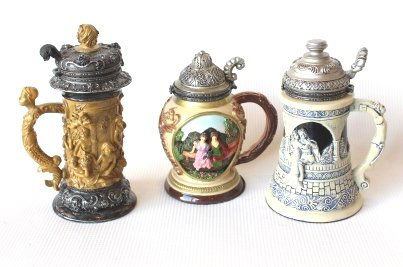 Lot of Three Mini Beer Steins: 1. Cherubs- Signed Nini. Made of Ceramic. Approximately measuring 6 x 3.5 x 3 Colorings include tan and silver 2. Roman/Clamshell. Made of ceramic. Approximately measuring 5.5 x 3.5 x 3.5. Colorings i