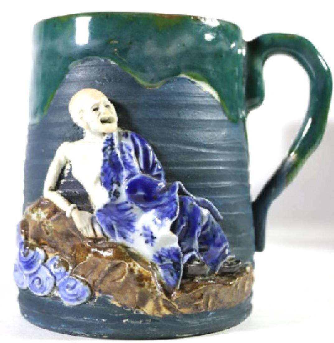 JAPANESE OVERSIZED SUMIDA GAWA MUG: Large Japanese Sumida gawa mug with applied figure of reclining Buddhist lohan (saint). Blue and white seal of Ryosai. 5.5" x diameter 4.5"