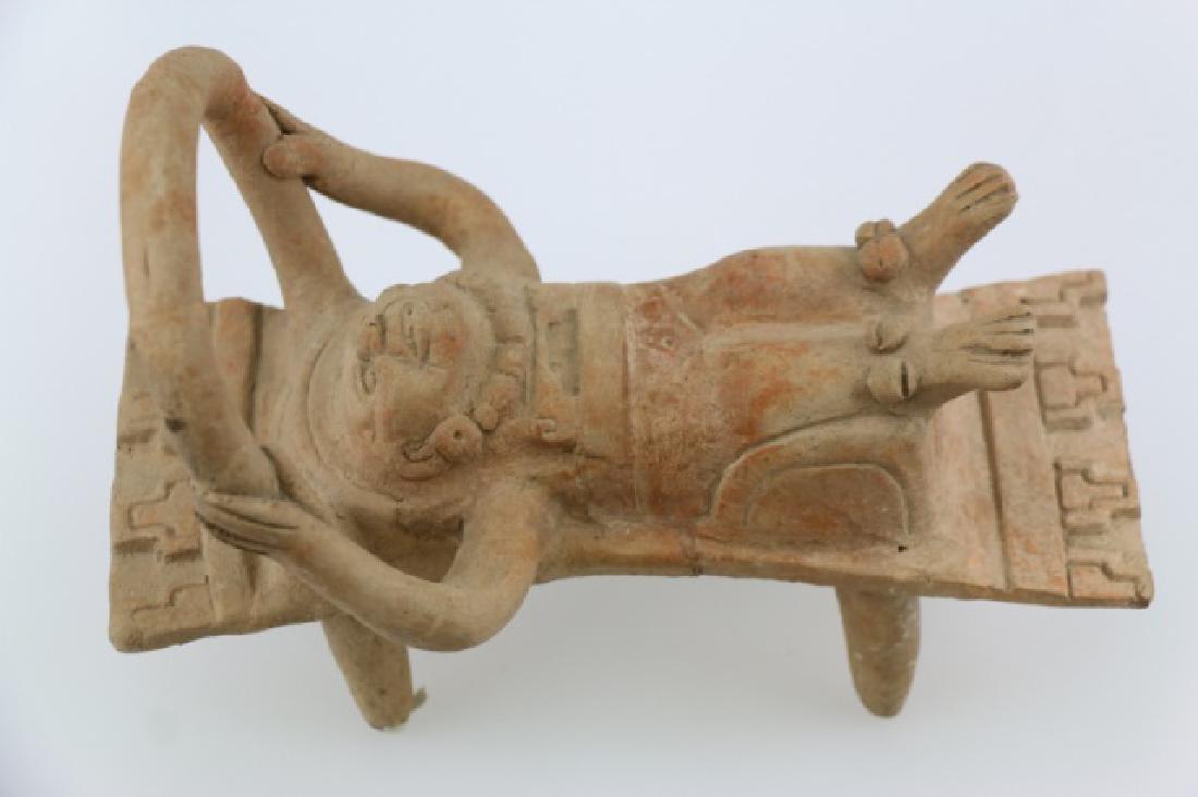 PRE-COLUMBIAN VERA CRUZ BEDDED FIGURE: PRE-COLUMBIAN VERA CRUZ BEDDED FIGURE, EARLY POST CLASSIC PERIOD, 10" L X 7 3/4" H. HOLLOW, MOLD MADE TERRACOTTA, HUMAN FIGURE WITH SOLID SCULPTED ARMS ABOVE HEAD HOLDLING ON TO A LARGE OPEN YOKE-TYPE