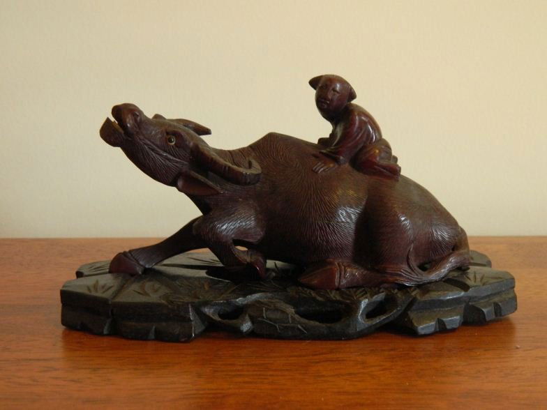 Oriental carving of ox lying down with man on ox's: Oriental carving of ox lying down with man on ox's back; mounted on an ebony base