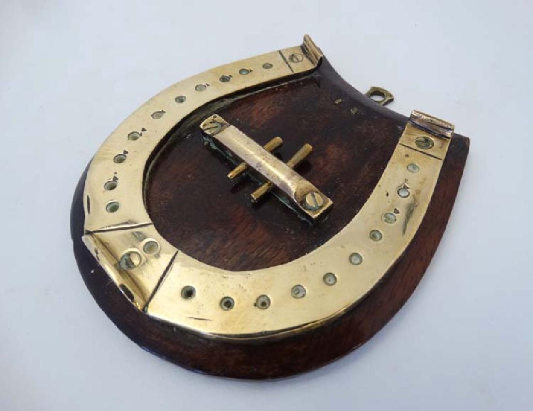 A small brass cribbage board formed as a horseshoe,: A small brass cribbage board formed as a horseshoe, with two pegs and mounted upon a wooden plinth. 4'' high.
