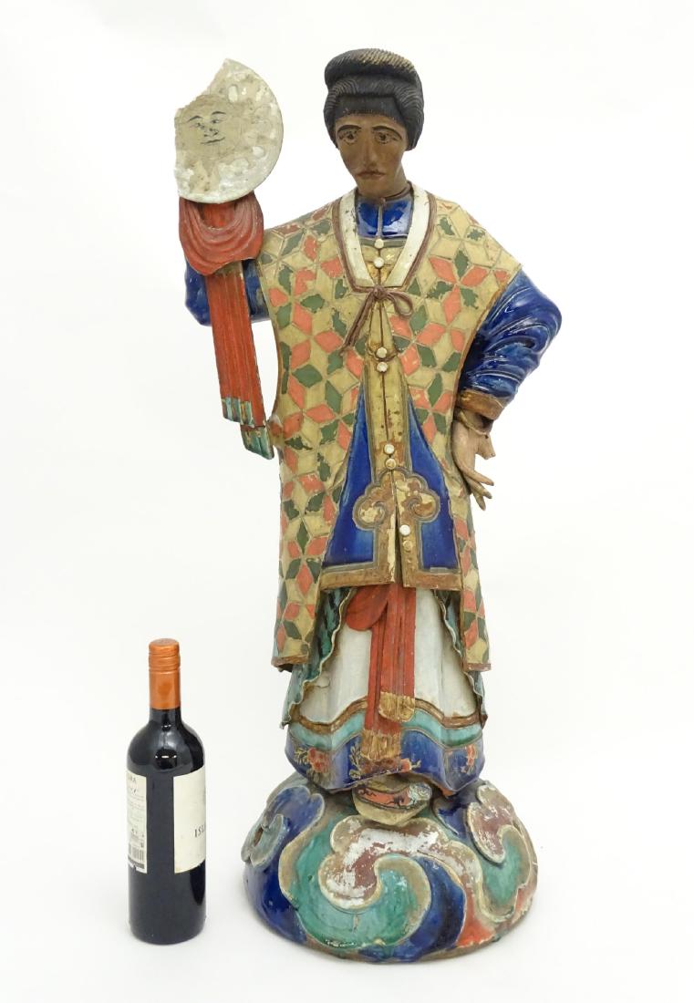 A tall Chinese ceramic figure wearing robes and holding: A tall Chinese ceramic figure wearing robes and holding a roundel in one hand having a sun to centre , standing 33'' high
