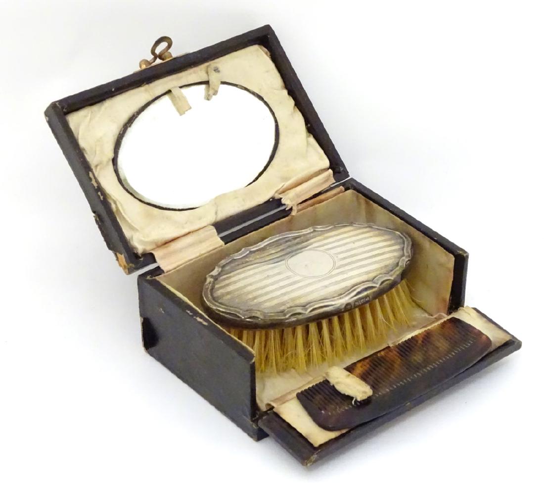 A travelling set comprising comb, brush and mirror, the: A travelling set comprising comb, brush and mirror, the brush with silver back hallmarked Chester 1927 maker W J Myatt & Co. The case 4 1/2'' wide