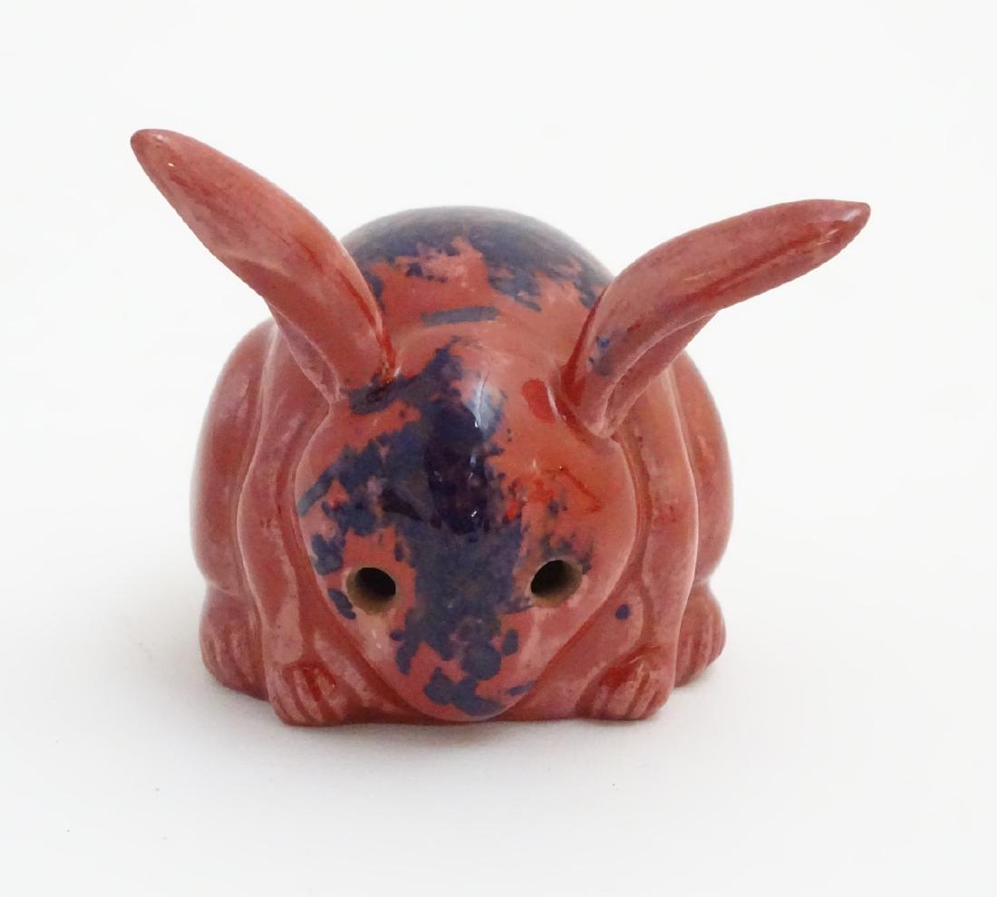 A Bernard Moore model of a rabbit in a red flambe glaze: A Bernard Moore model of a rabbit in a red flambe glaze with high fired blue patches to face and back, painted BM monogram to interior of base. Approx. 2 3/4'' high.