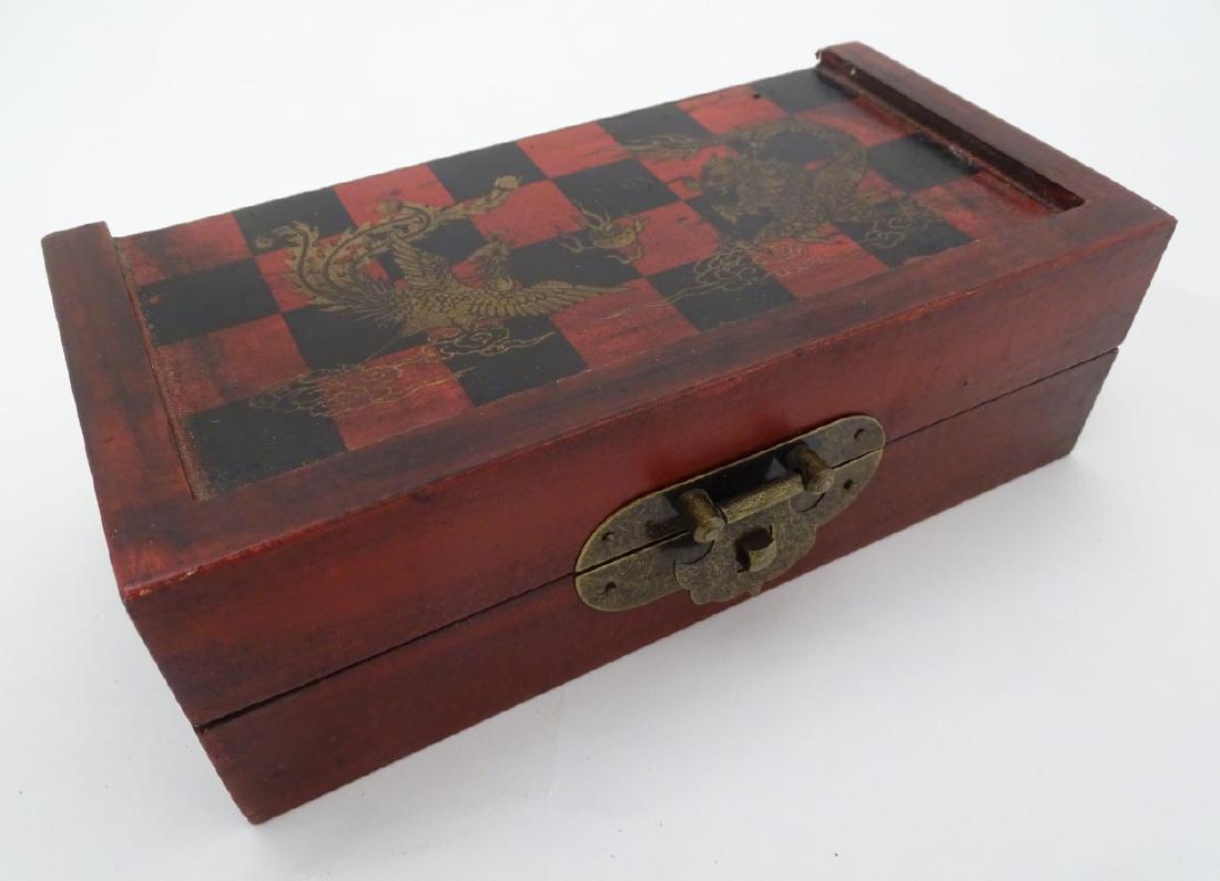 A Chinese travelling wooden chess set with red and: A Chinese travelling wooden chess set with red and black chequer board with Chinese dragon motifs, containing the 32 piece white and red/black chess pieces, the castles being of round turret design an
