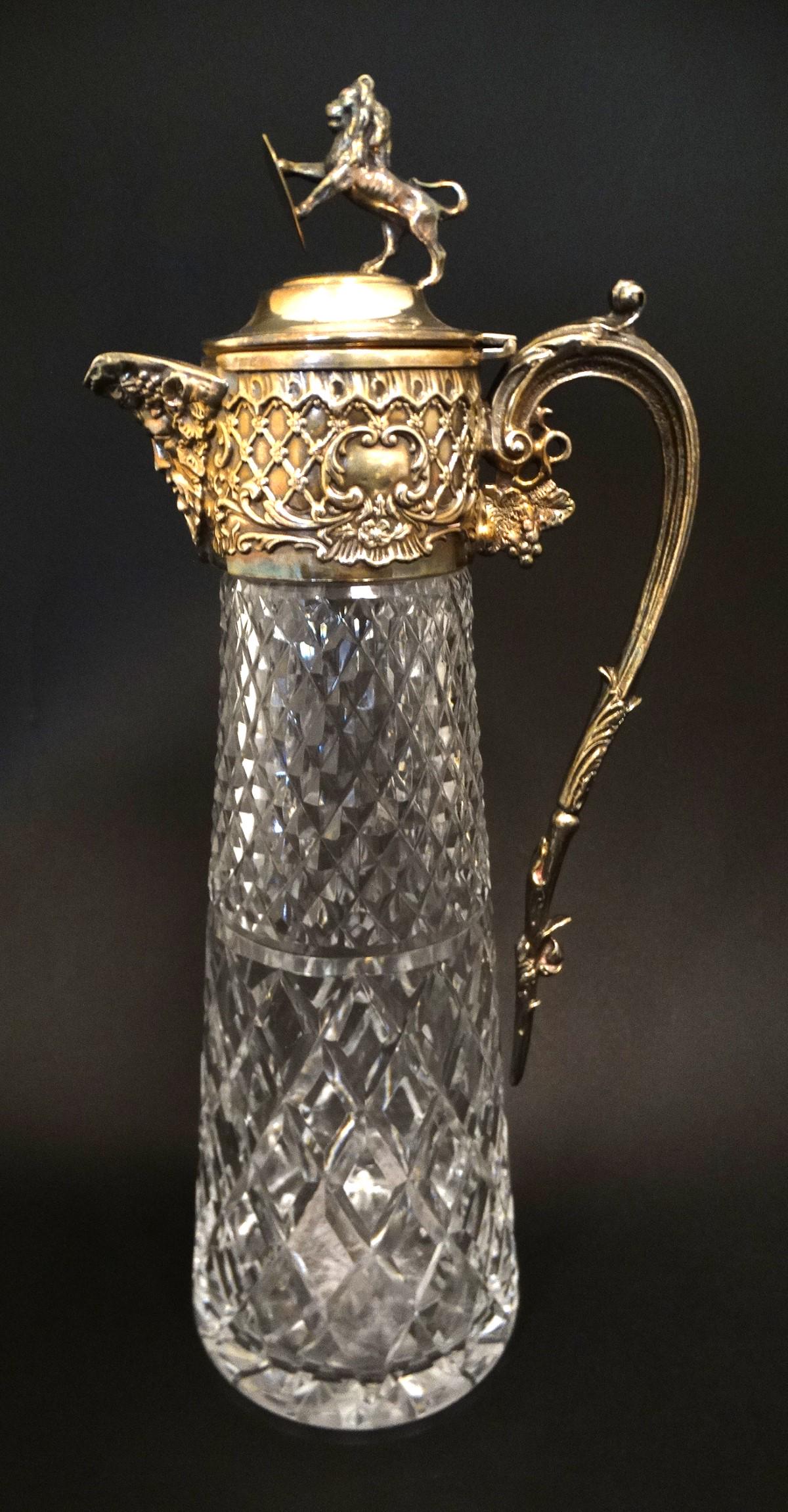 Glass : a claret jug with silver plate top and hinged: Glass : a claret jug with silver plate top and hinged lid ( with rampant lion holding a shield to top, Rococo , Bacchus and grapevine decoration , the glass body with hobnail cut decoration ,measuring
