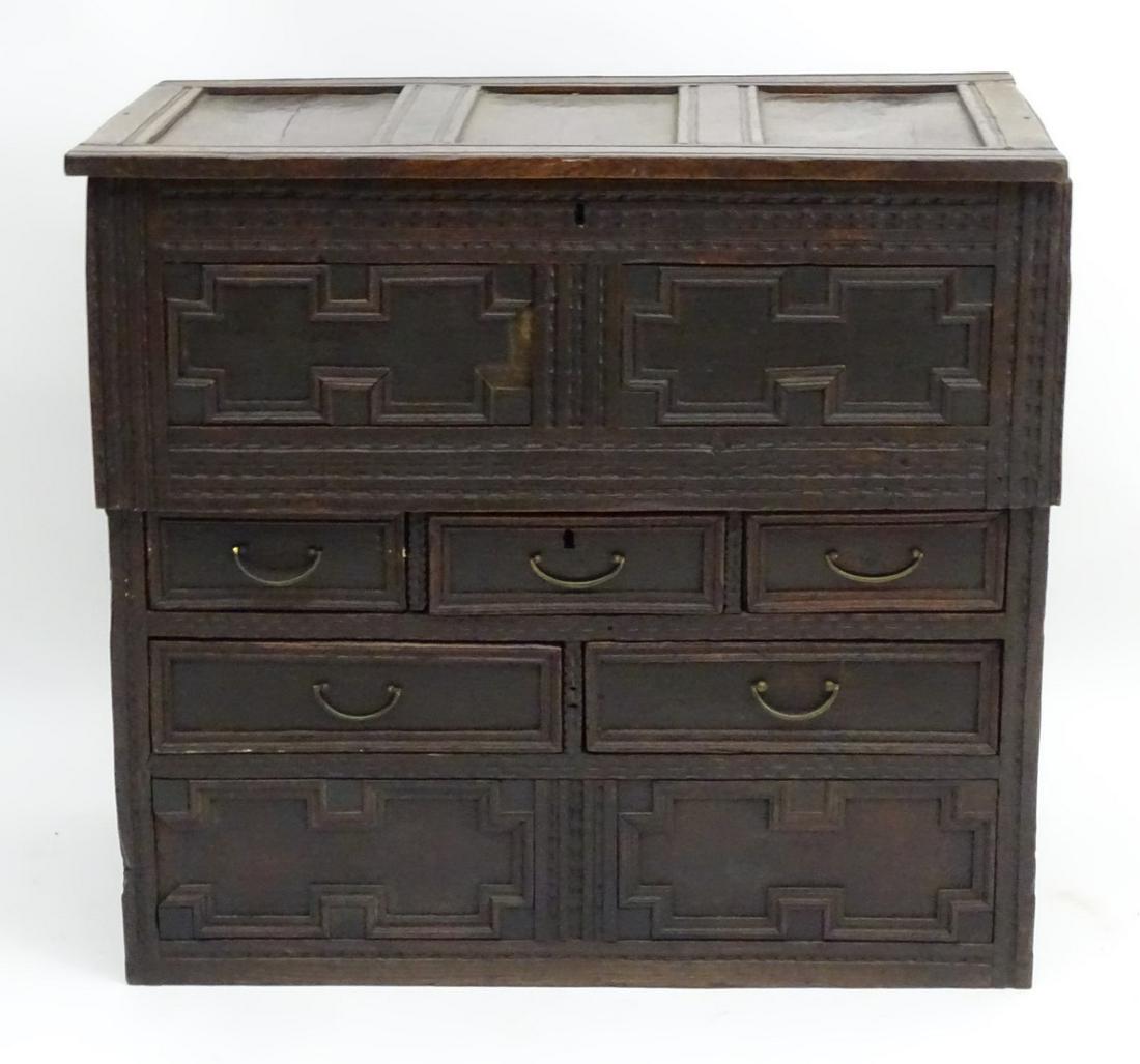 An 18thC and later oak chest with a panelled lid above: An 18thC and later oak chest with a panelled lid above a carcass having geometric mouldings and carved decoration, the chest comprising five short drawers. 38'' long x 23'' wide x 35 ½'' high
