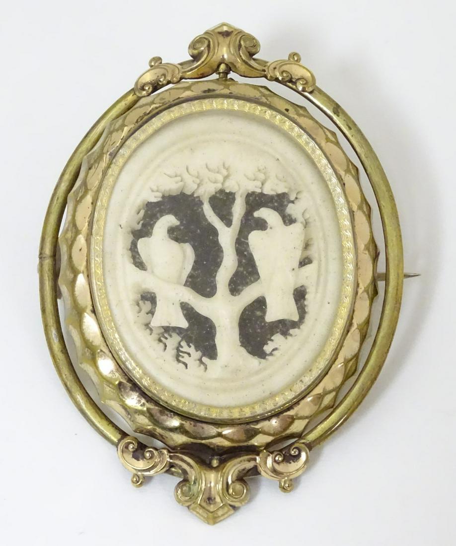 A Victorian brooch having central glazed locket section: A Victorian brooch having central glazed locket section containing carved scene of birds of prey in a tree, the whole within a pinch beck / gilt metal surround. 2 3/4'' long