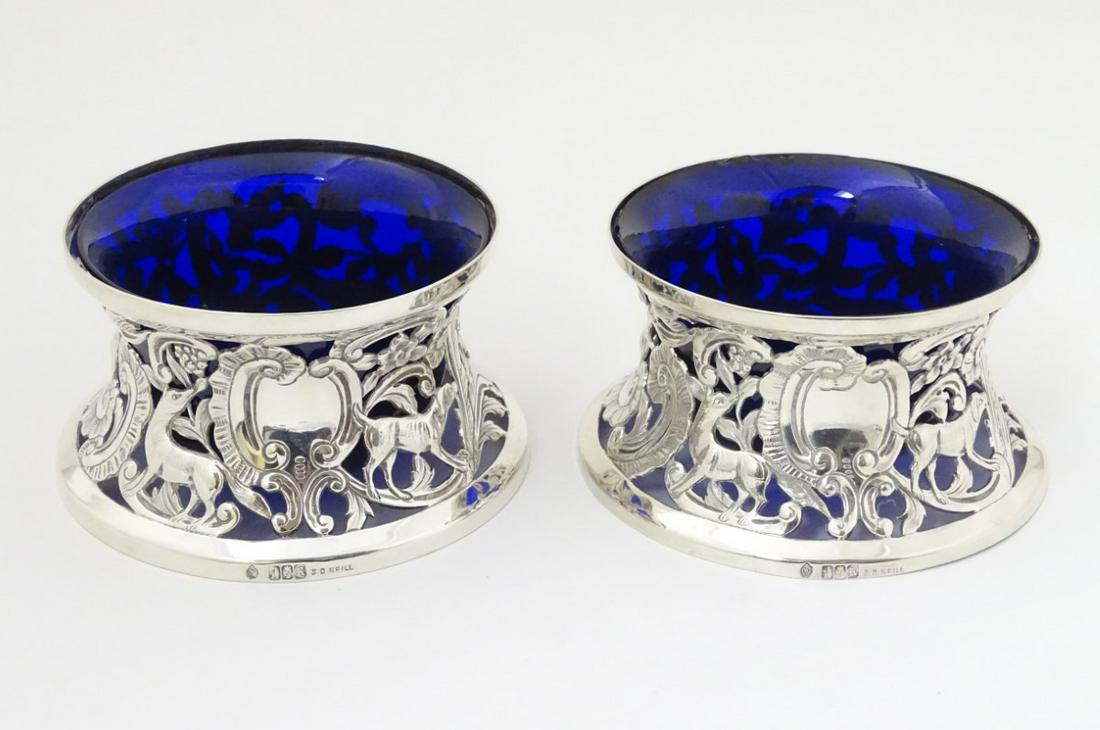 A pair of Irish silver potato rings with ornate pierced: A pair of Irish silver potato rings with ornate pierced scroll, floral and dog decoration. Hallmarked Dublin 1912 maker Sharman D Neill. with blue glass liners. 4 1/2'' wide (228g)