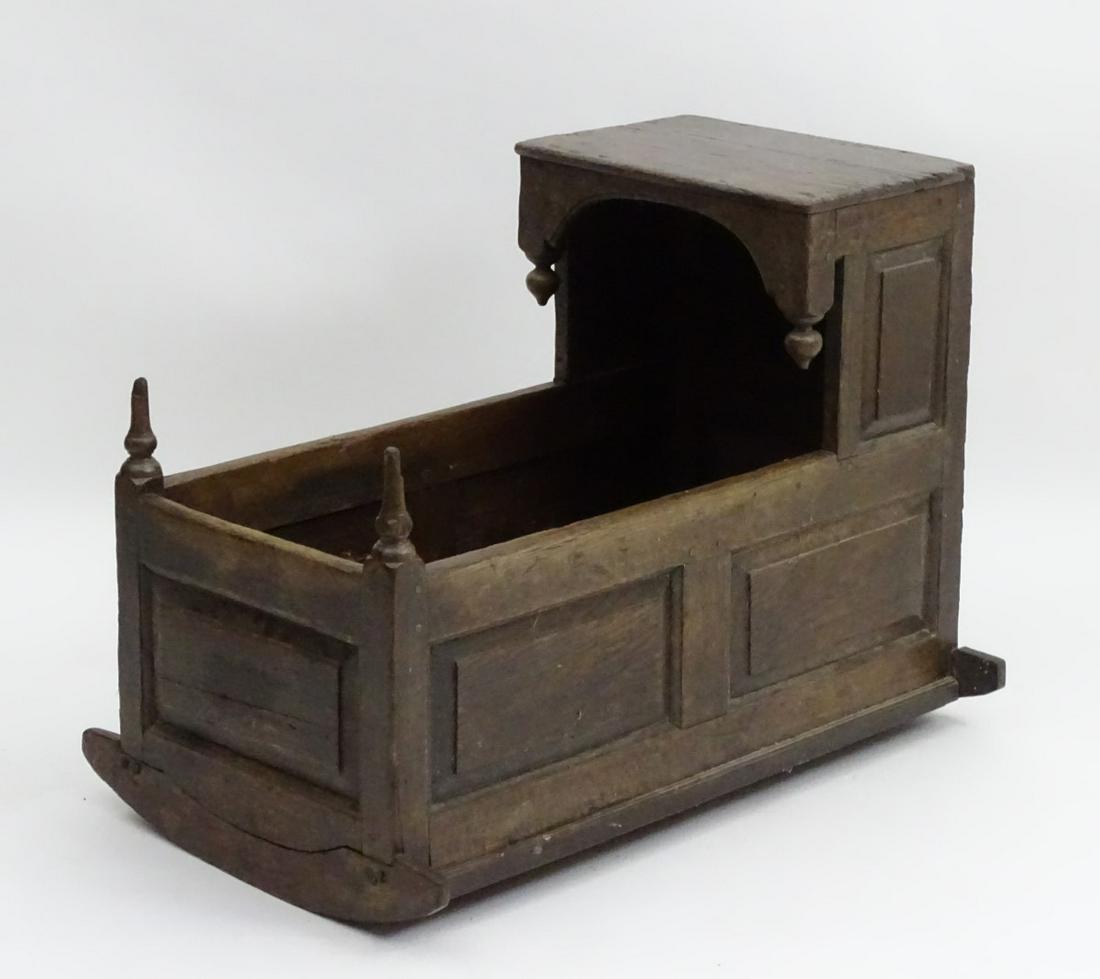 An 18thC / 19thC oak crib with an overhanging hood and: An 18thC / 19thC oak crib with an overhanging hood and decorative hanging finials, the panelled peg jointed carcass raised on rocking sleighs. 37'' long x 22'' wide x 28'' high