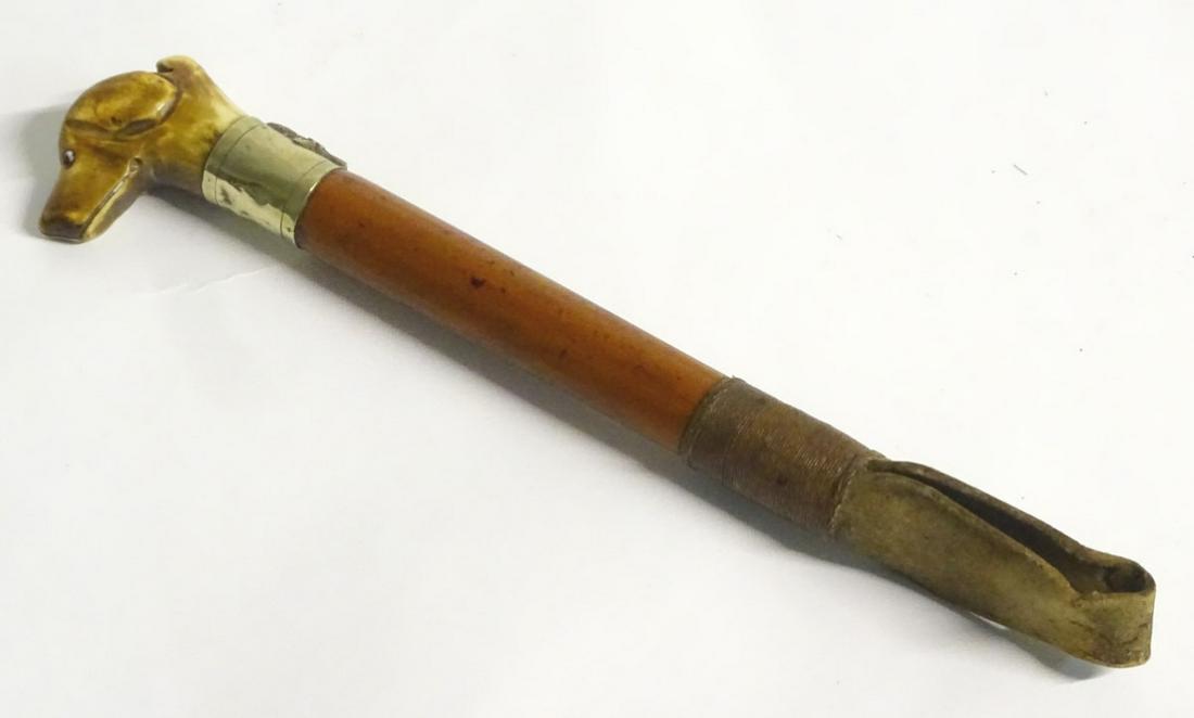 Hunting: An early 20thC Harriers crop, with a carved: Hunting: An early 20thC Harriers crop, with a carved antler whistle top, formed as the head of a hound with glass eyes, a silver plate collar and a malacca shaft. Approx. 11 ½'' long.