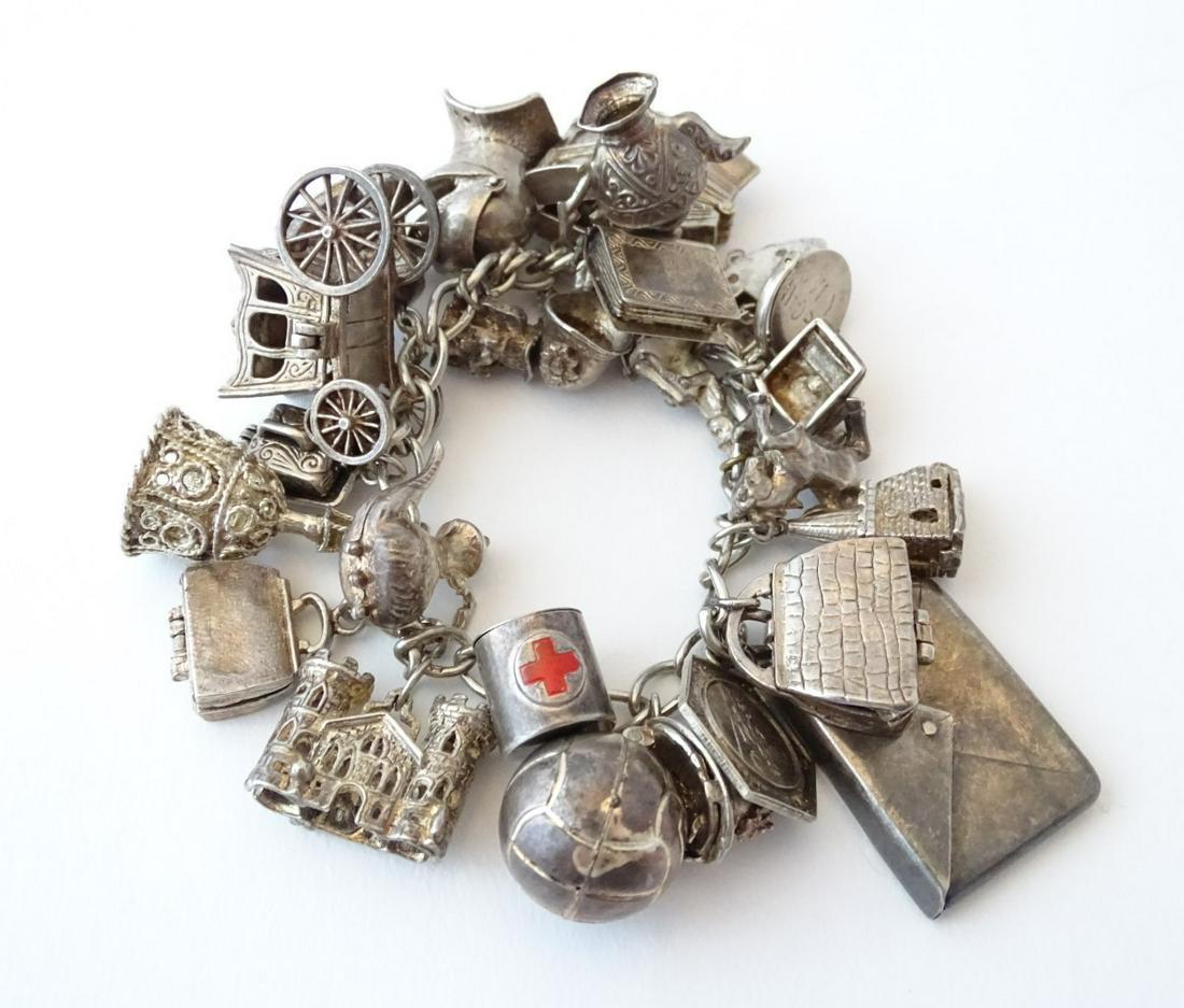 A silver and white metal charm bracelet with various: A silver and white metal charm bracelet with various charms including a silver carriage, knights armour helmet, bag, , hat, typewriter, church, horse and a silver stamp case of envelope form. Total we