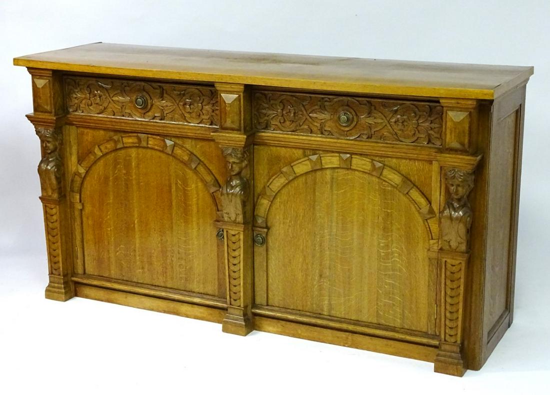 A mid 20thC oak sideboard with a rectangular top above: A mid 20thC oak sideboard with a rectangular top above two frieze drawers with decorative carving and ring pull handles, the two panelled cupboards separated by caryatid supports and stepped plinth ba