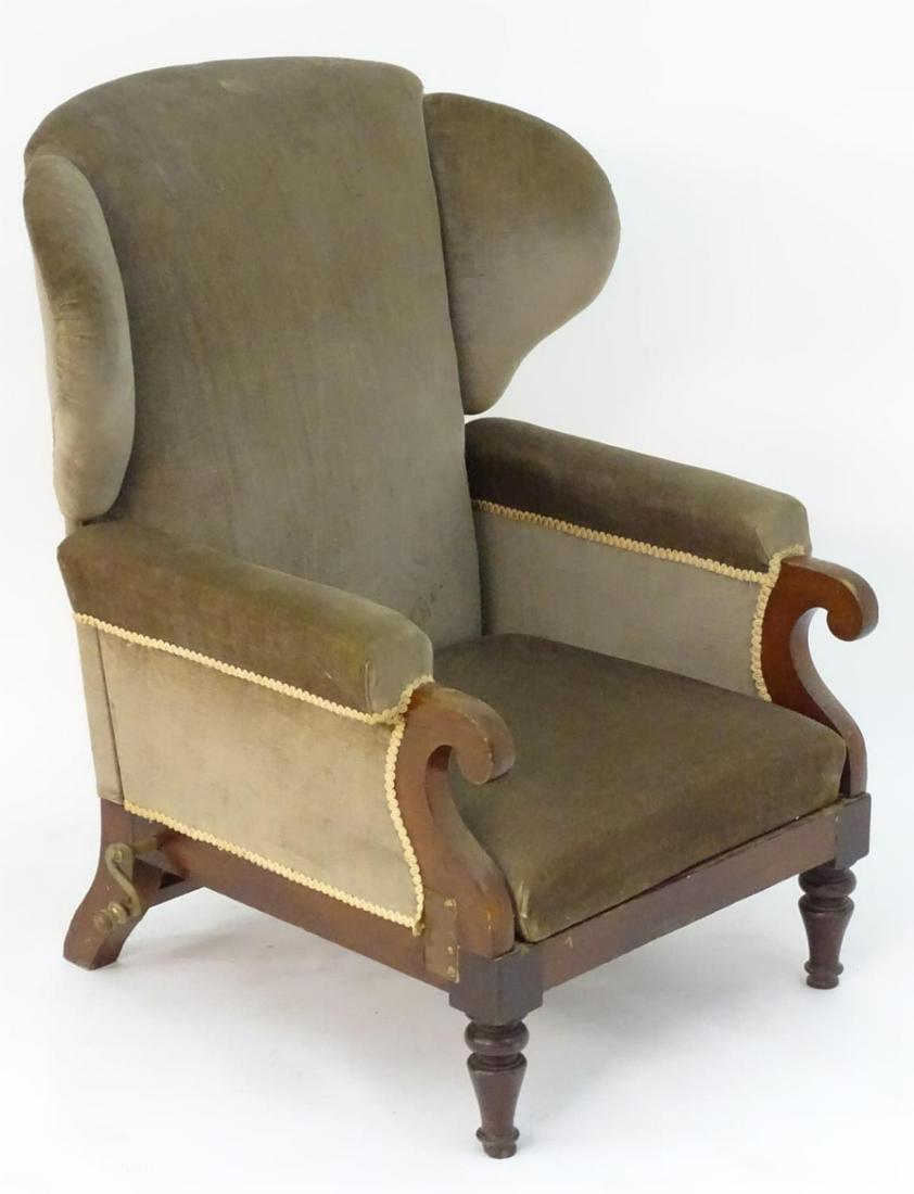 A Victorian wingback adjustable armchair with scrolled: A Victorian wingback adjustable armchair with scrolled arms, mechanical crank to one side and raised on turned front legs and block back legs. Bearing label 'John Ward. Manufacturer to the King and Ro