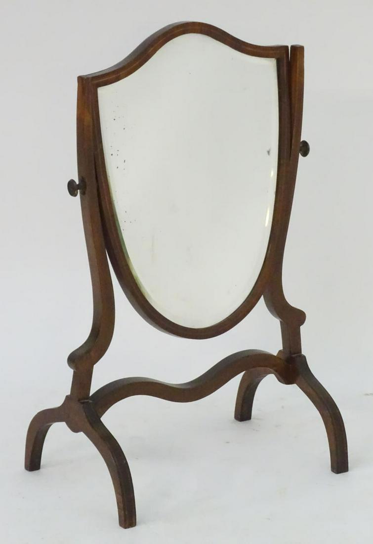 A 19thC shield shaped dressing table mirror with: A 19thC shield shaped dressing table mirror with satinwood stringing to the frame, raised on shaped legs with a supporting stretcher. 16" wide x 11" deep x 27" high.