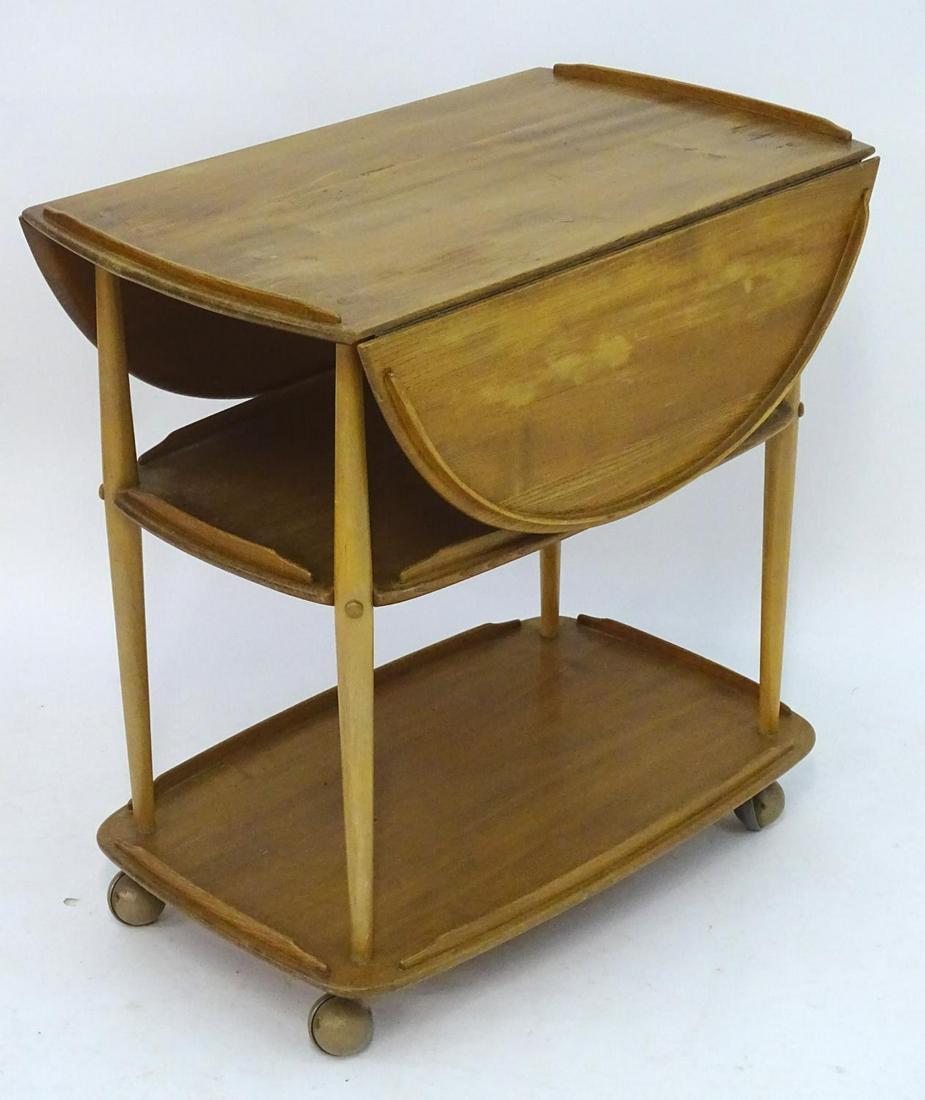 Vintage Retro, Mid-Century: an Ercol elm and beech: Vintage Retro, Mid-Century: an Ercol elm and beech three tiered trolley, the top with drop flaps, supported by four tapered columns and standing on ball feet. 30" tall, 29" long, 18 1/2 wide