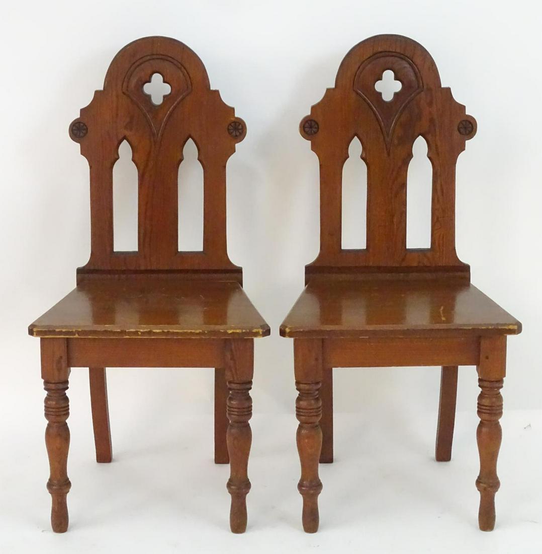 A pair of late 19thC pine Gothic chairs with quatrefoil: A pair of late 19thC pine Gothic chairs with quatrefoil decoration and pierced lancet decoration, the chairs raised on turned tapering front legs and splayed back legs. 20" wide x 16" deep x 39" high.