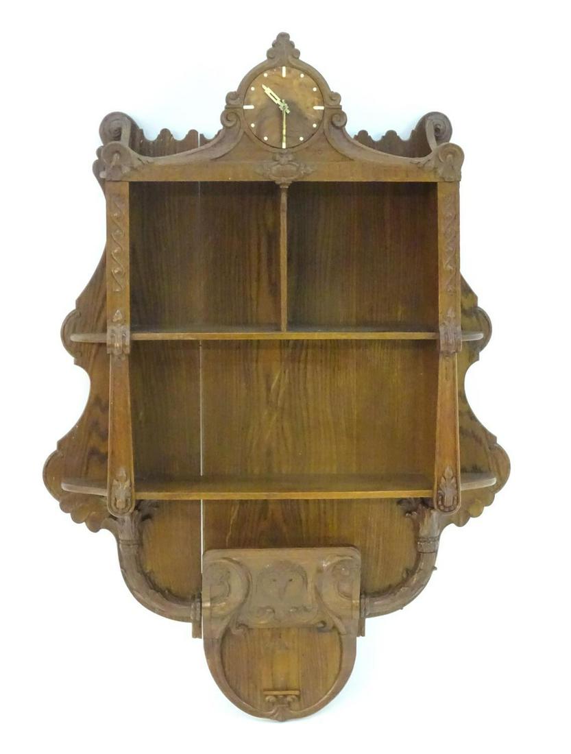 A c.1936 oak hanging shelf with a carved frame, walnut: A c.1936 oak hanging shelf with a carved frame, walnut clock face, graduated shelves and a carved owl motif. 33" wide x 48" high.