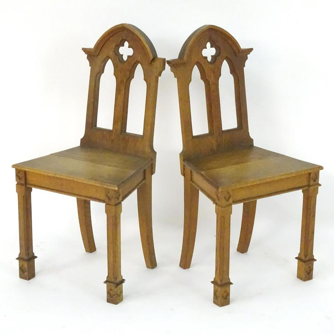 A pair of mid 19thC oak hall chairs with pointed: A pair of mid 19thC oak hall chairs with pointed pediments, pierced decoration and carved quatrefoils above squared front legs and sabre back legs. 18" wide x 14 1/2" deep x 36" high.