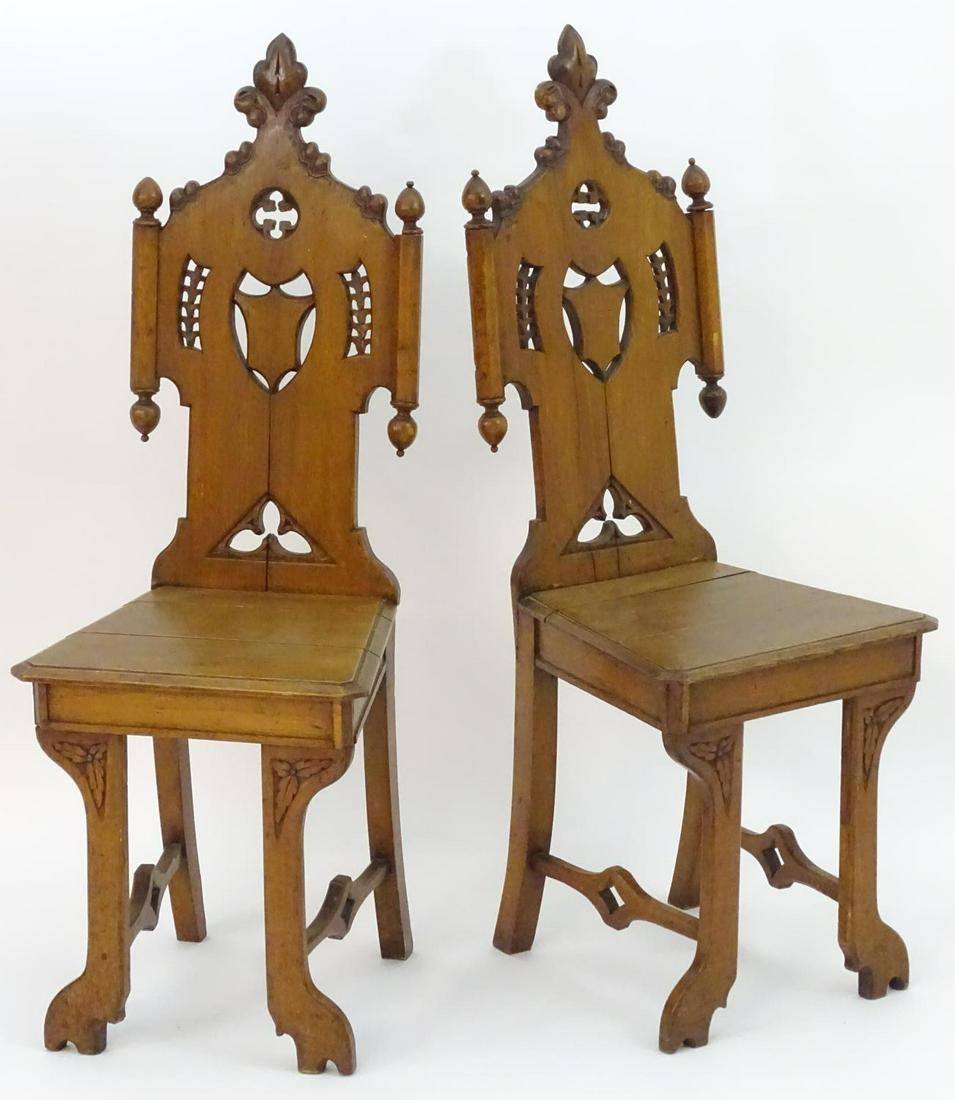 A pair of 19thC oak hall chairs with carved backrests,: A pair of 19thC oak hall chairs with carved backrests, pierced quatrefoil decoration and a shield to the centre, having a chamfered frame, shaped legs and pierced stretchers. 16" wide x 18" deep x 43"