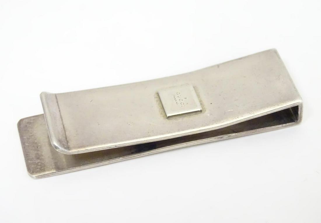A silver money clip engraved ' Gucci ' to top. Approx: A silver money clip engraved ' Gucci ' to top. Approx 2" long Category Silver & Silver-plated items