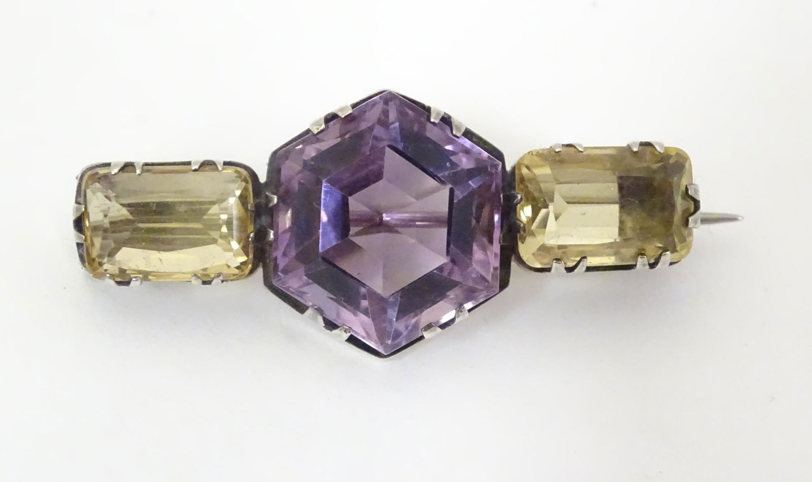 A white metal brooch set with central amethyst flanked: A white metal brooch set with central amethyst flanked by citrine in an Art Deco style setting. 1 1/2" wide