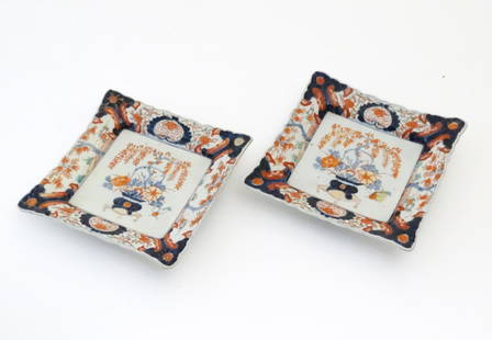 A pair of Japanese plates of square form decorated in the Imari palette with a vase of flowers and: A pair of Japanese plates of square form decorated in the Imari palette with a vase of flowers and foliage on a scrolled stand. The borders decorated with blossoming trees. The reverse with blue