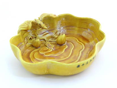 A Chinese fluted edged yellow brush wash dish with relief bat and fruit decoration. Character marks: A Chinese fluted edged yellow brush wash dish with relief bat and fruit decoration. Character marks to side. Approx. 1 3/4" high x 6" wide x 5 1/4" deep