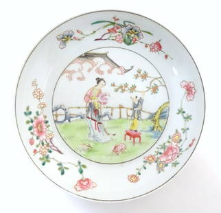 A Chinese famille rose plate decorated with a woman holding a fan in a garden terrace with a young: A Chinese famille rose plate decorated with a woman holding a fan in a garden terrace with a young attendant, two stylised rabbits and a pagoda style building amongst clouds beyond. The border with