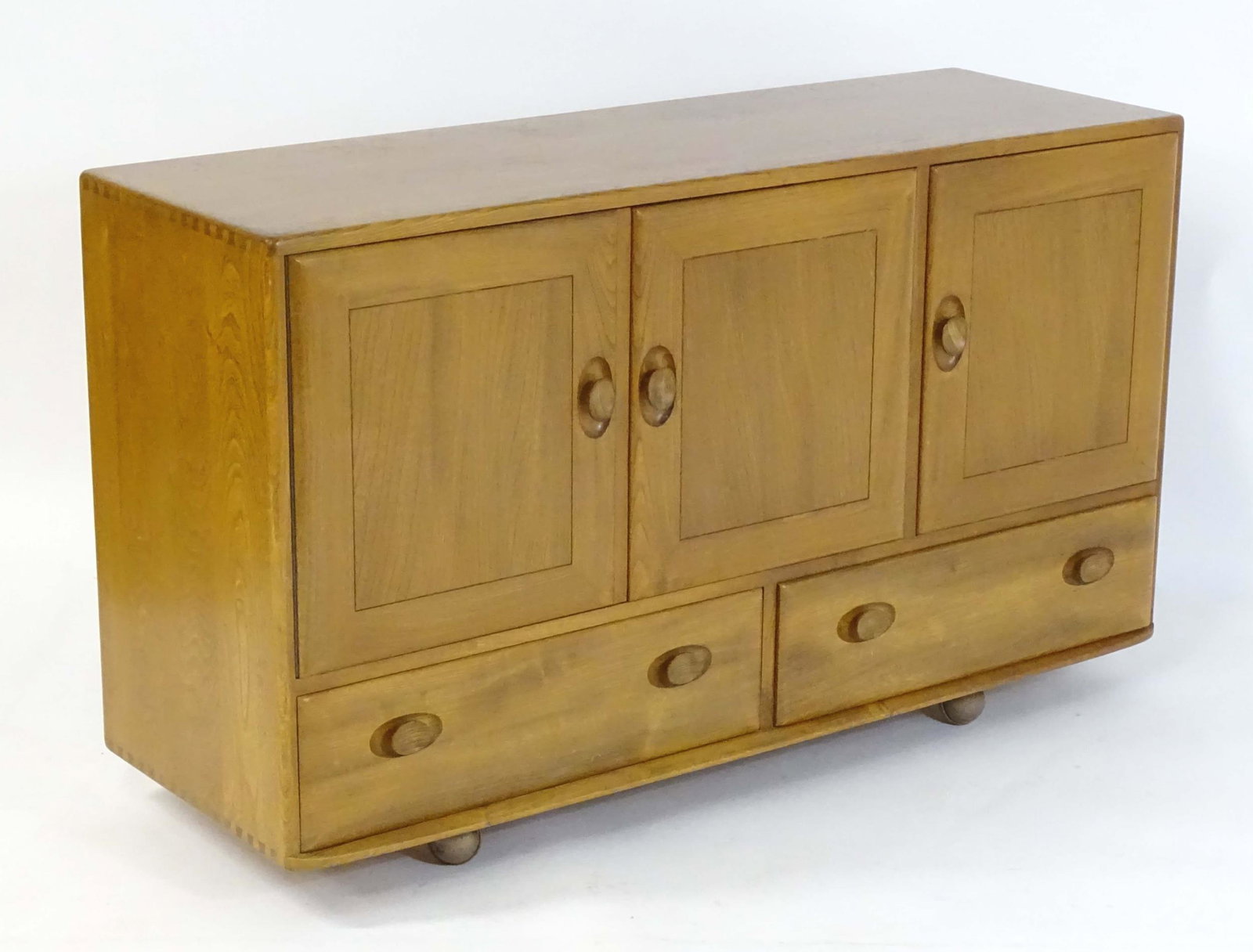 Vintage / Retro: An Ercol sideboard of elm construction with exposed dovetailing and comprising: Vintage / Retro: An Ercol sideboard of elm construction with exposed dovetailing and comprising three cupboards above two drawers and raised on four castors. 51" wide x 17" deep x 30" high.