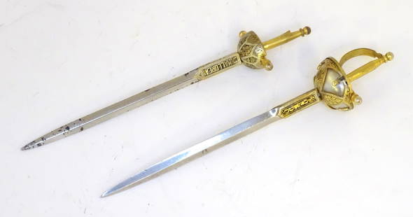 Militaria : two 20thC novelty / souvenir letter openers formed as cup hilt rapier swords, each with: Militaria : two 20thC novelty / souvenir letter openers formed as cup hilt rapier swords, each with gilt decoration and named Mallorca and Toledo. The larger example 7" long