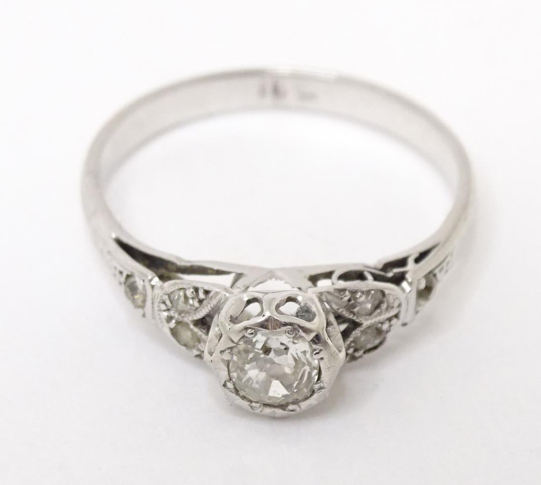 An 18ct white gold ring set with central diamond flanked by further diamonds to shoulders. Ring size (1 of 6)